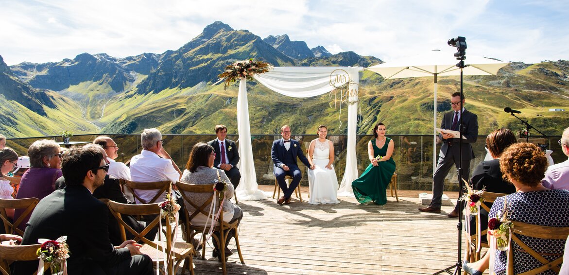 Die Gäste und das Brautpaar während der Trauung auf der Terrasse der Vinnova mit unglaublichen Ausblick auf die dahinterliegende Bergwelt | © Silvretta Montafon - Stefan Kothner