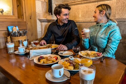 Bergfrühstück - Silvretta Montafon | © Vanessa Strauch - Silvretta Montafon Ein Pärchen sitzt beim Bergfrühstück bei gedecktem Tisch in einer Berghütte. | © Vanessa Strauch - Silvretta Montafon