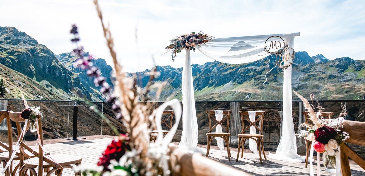 Dekorierter Traubogen und Bestuhlung für eine Hochzeit auf der Terrasse der VINNOVA mit Berge im Hintergrund | © Silvretta Montafon - Patrick Säly