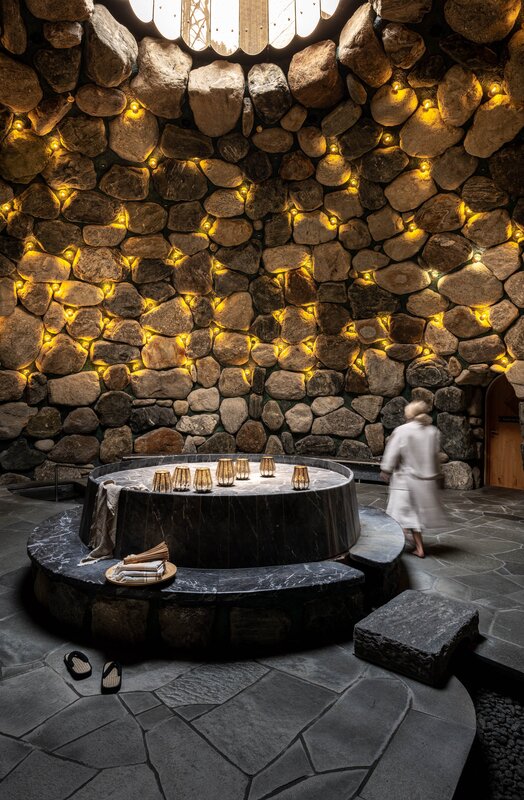 Gold Spa im Sporthotel Silvretta Montafon | © Silvretta Montafon - blateral Eine Frau läuft durch das Tepidarium, welches in goldenes Licht getaucht ist mit einem Loch in der Decke.  | © Silvretta Montafon - blateral
