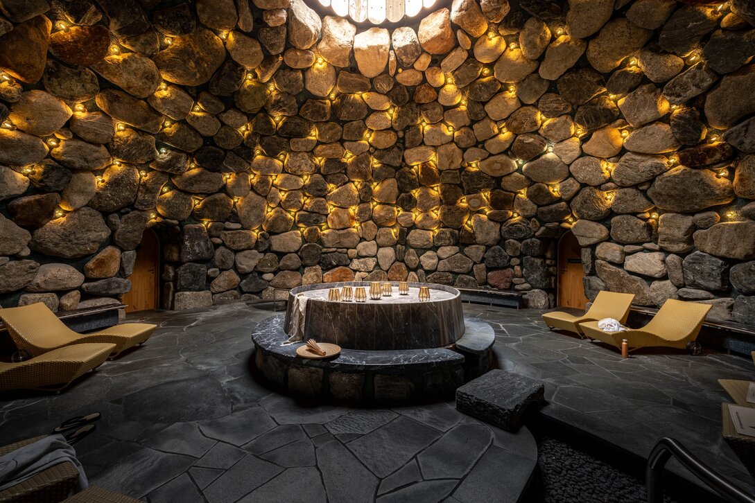 Gold Spa im Sporthotel Silvretta Montafon | © Silvretta Montafon - blateral Das Tepidarium mit goldenem Licht an den Steinwänden und einem Loch in der Decke | © Silvretta Montafon - blateral