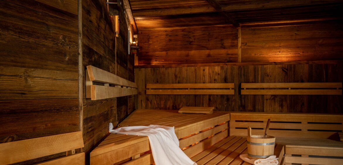 Finnische Sauna mit Holzwänden und Holzbänken auf denen ein Handtuch und eine Wasserschale aus Holz stehen | © Silvretta Montafon - blateral