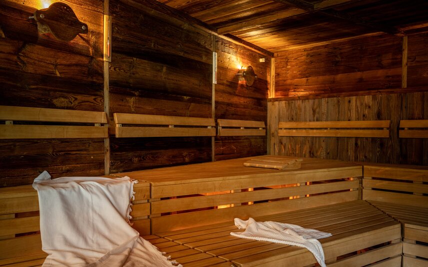 Gold Spa im Sporthotel Silvretta Montafon | © Silvretta Montafon - blateral Eine finnische Sauna mit Holzwänden und Holzbänken, auf welchem ein weißes Handtuch liegt und ein Wasserkübel aus Holz steht | © Silvretta Montafon - blateral