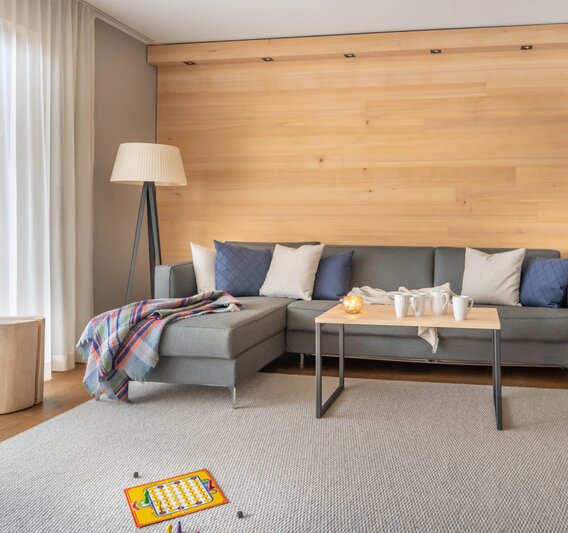 Sporthotel Chalet Silvretta Montafon | © Silvretta Montafon - blateral Eine große graue Couch auf einem hellgrauen Teppich und einem Mensch Ärger Dich Nicht Spiel im Vordergrund | © Silvretta Montafon - blateral