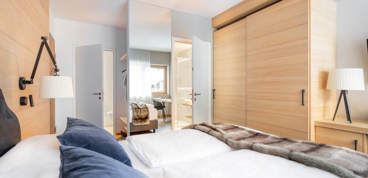 Ein Doppelbett mit grauer Polsterung und weißem Bettbezug und einer Felldecke drüber | © Silvretta Montafon - blateral