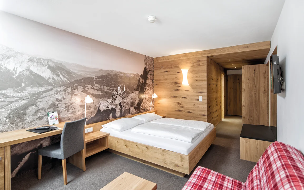 Doppelbett mit großem Schreibtisch und riesigem Wandposter | © Silvretta Montafon - Markus Gmeiner